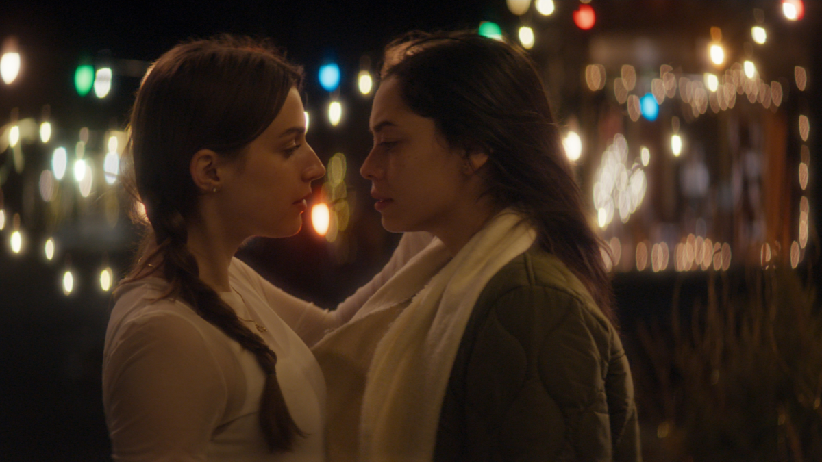 two girls face to face behind the christmas lights