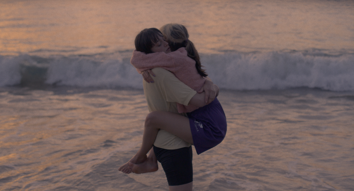 Stroking an Animal: one woman holds another woman with waves crashing behind them.