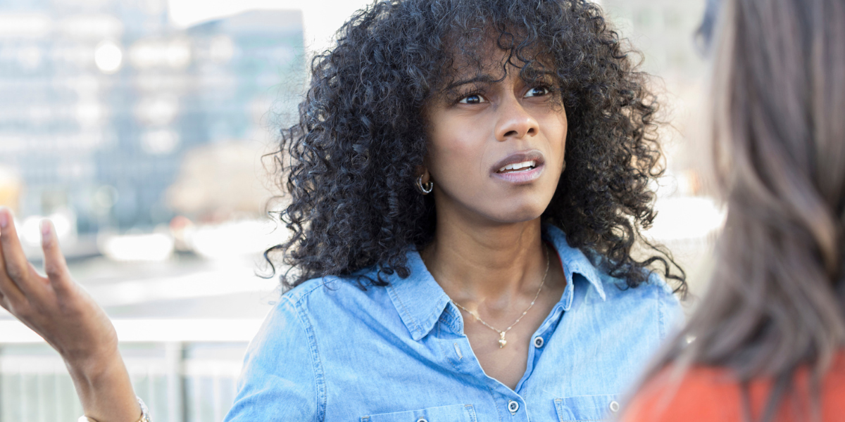 a woman with curly hair throws her arms up and frowns