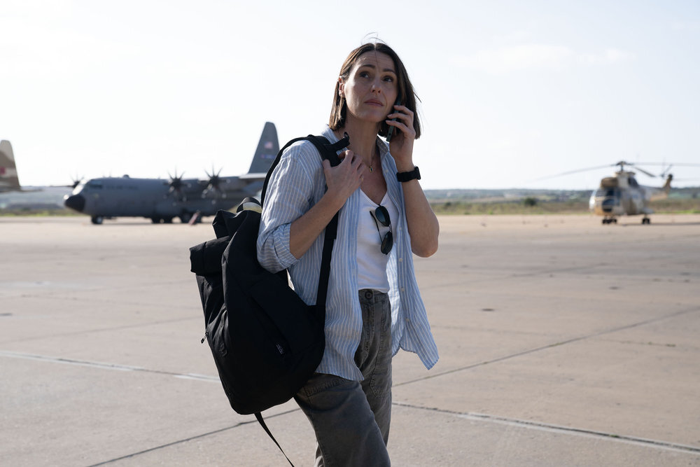 Suranne Jones stands on an airfield with a backpack and a phone