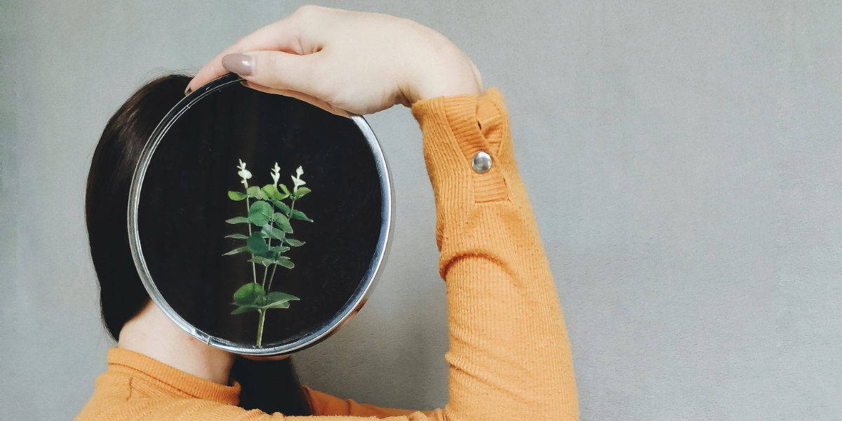 a woman holds a mirror to her head displaying wildflowers