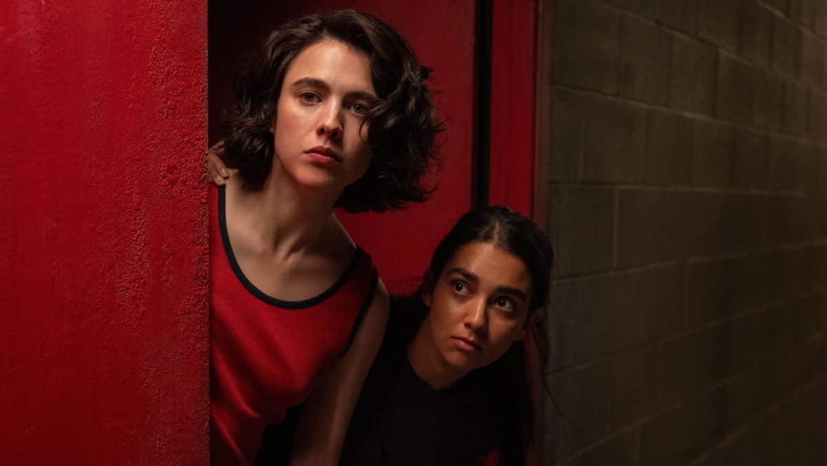 Margaret Qualley and Geraldine Viswanathan peak their heads around a doorway.