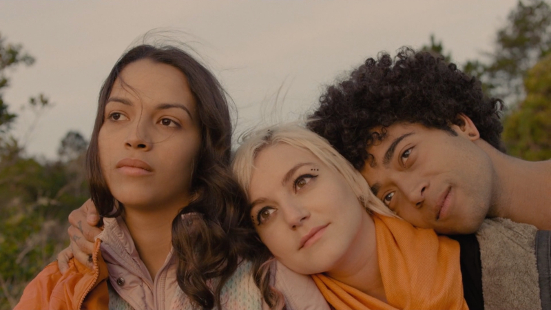 A teen boy and a teen girl lean their heads on another teen girl's shoulder as they watch the sunset