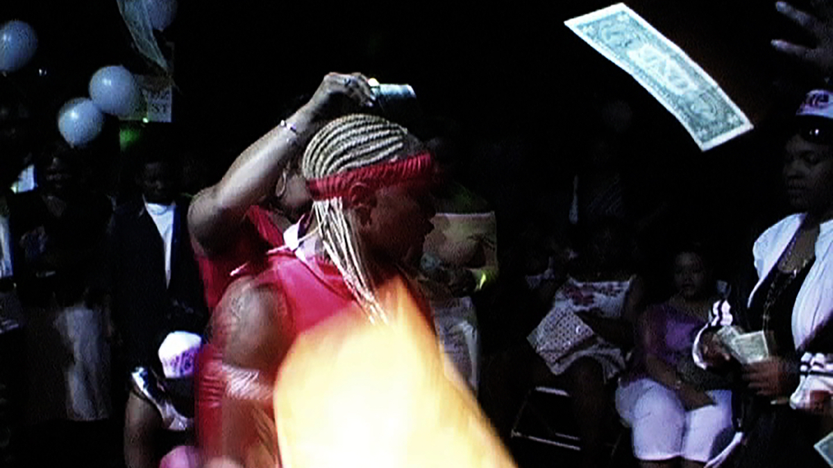 Studs and femmes dance at a club as a dollar bill floats in the air.