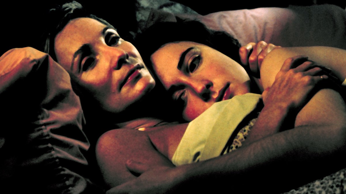 Two middle aged women lie in bed together. 