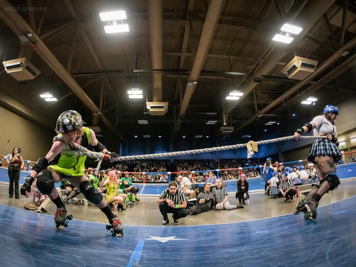 Two queers in skates play tug of war with a rope