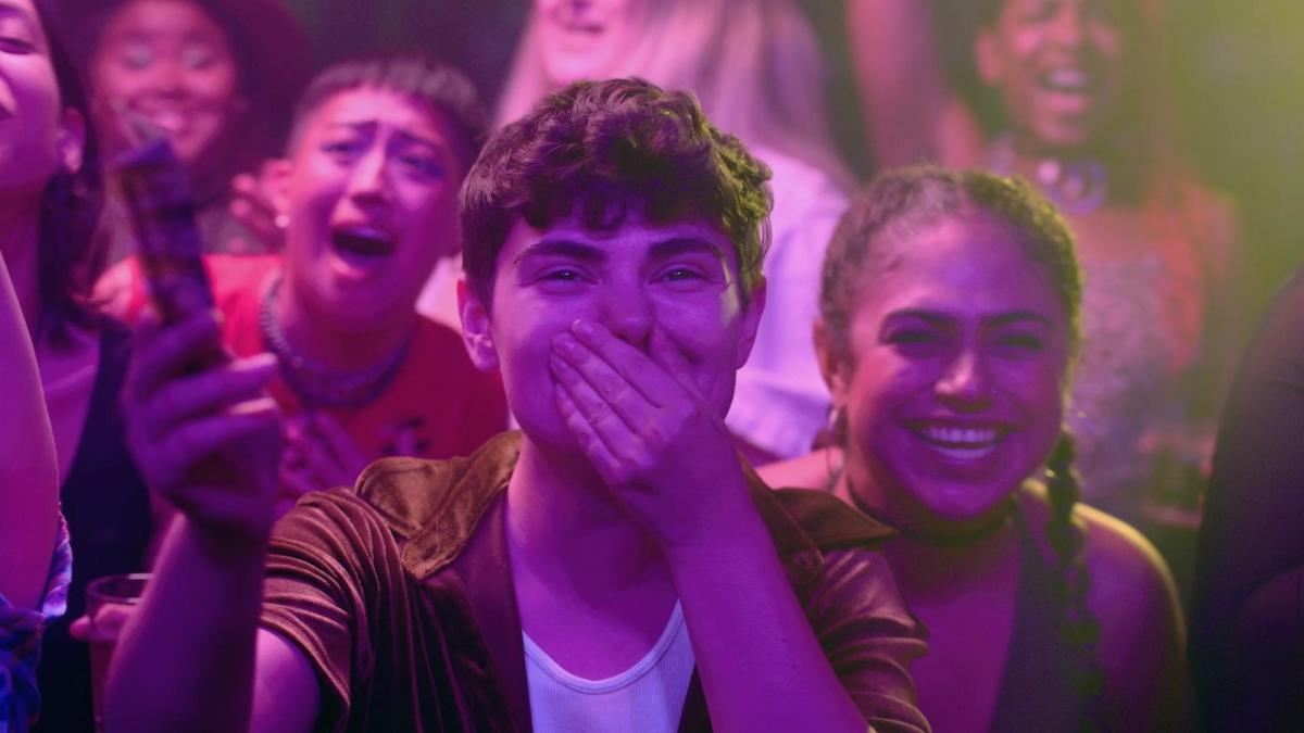 JJ Maley holds his face and laughs in a crowd awash in pink light.