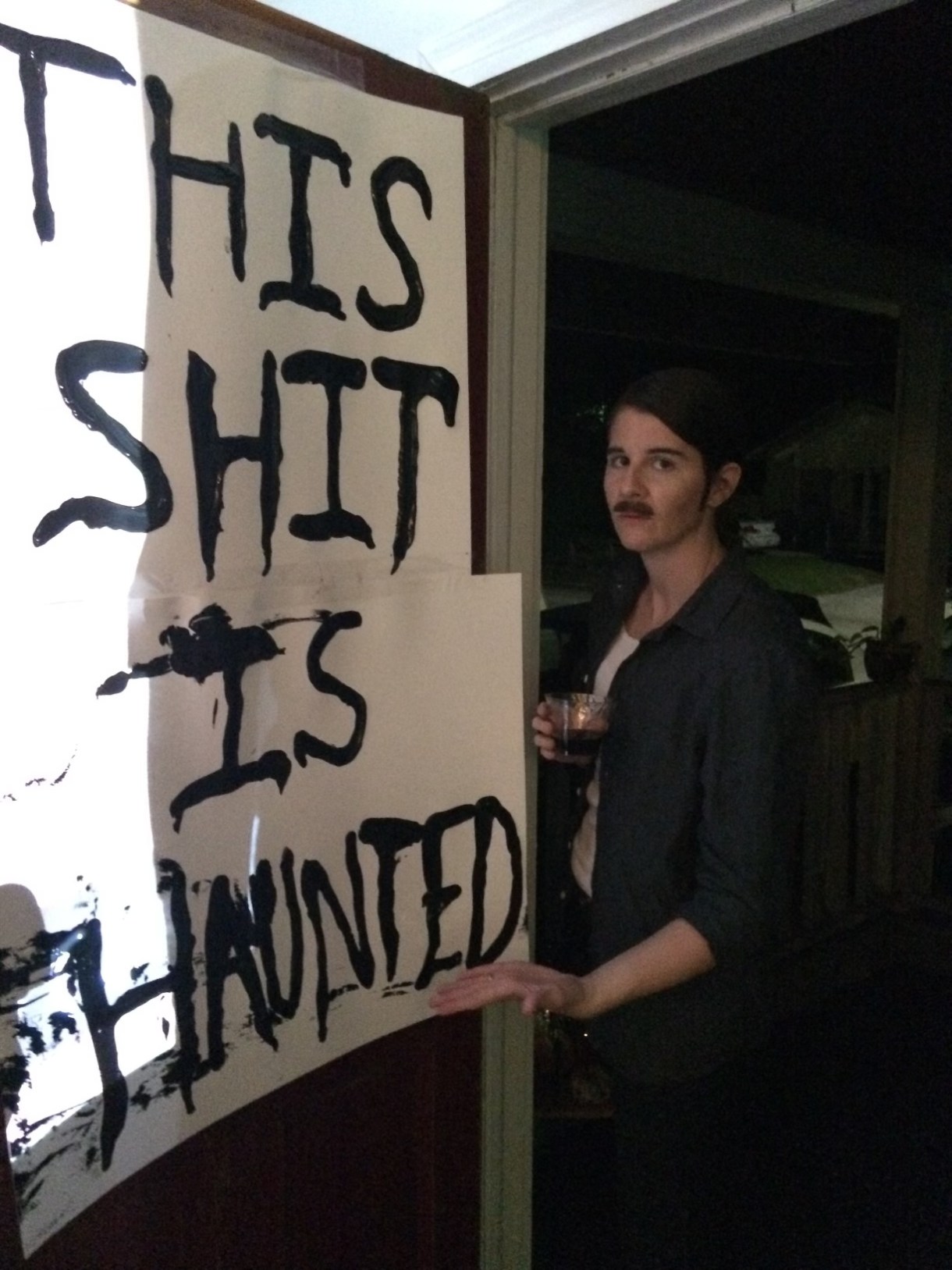 Kristen Arnett dressed as Lance from Portlandia next to a sign that says THIS SHIT IS HAUNTED