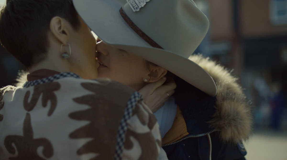 A woman in a cowboy hat kisses another woman.