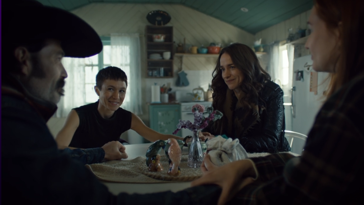 The main characters of Wynonna Earp sit around a table smiling.