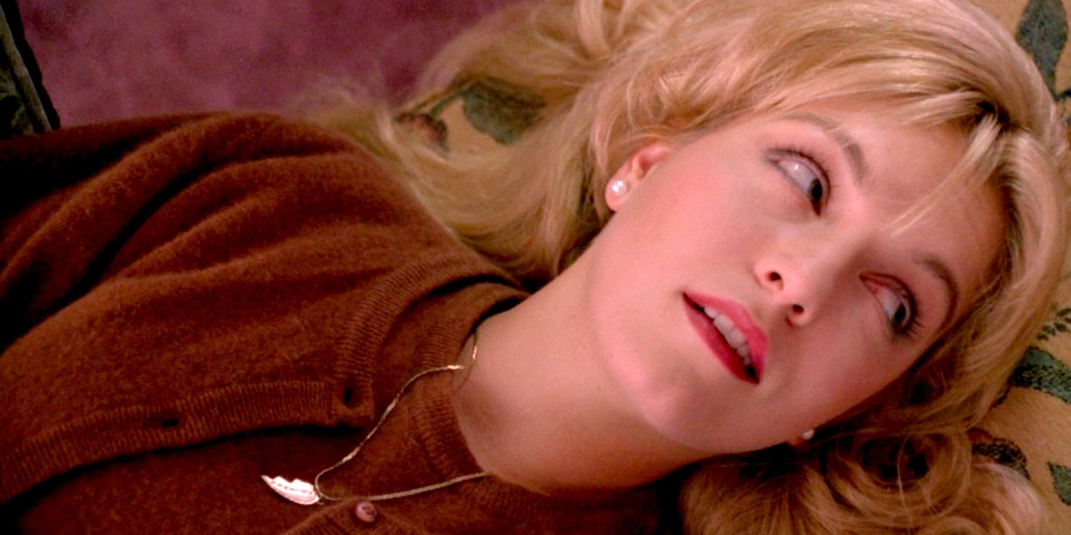 Laura Palmer smirks as she lies down and looks up with her signature half heart necklace on in David Lynch's Twin Peaks: Fire Walk With Me