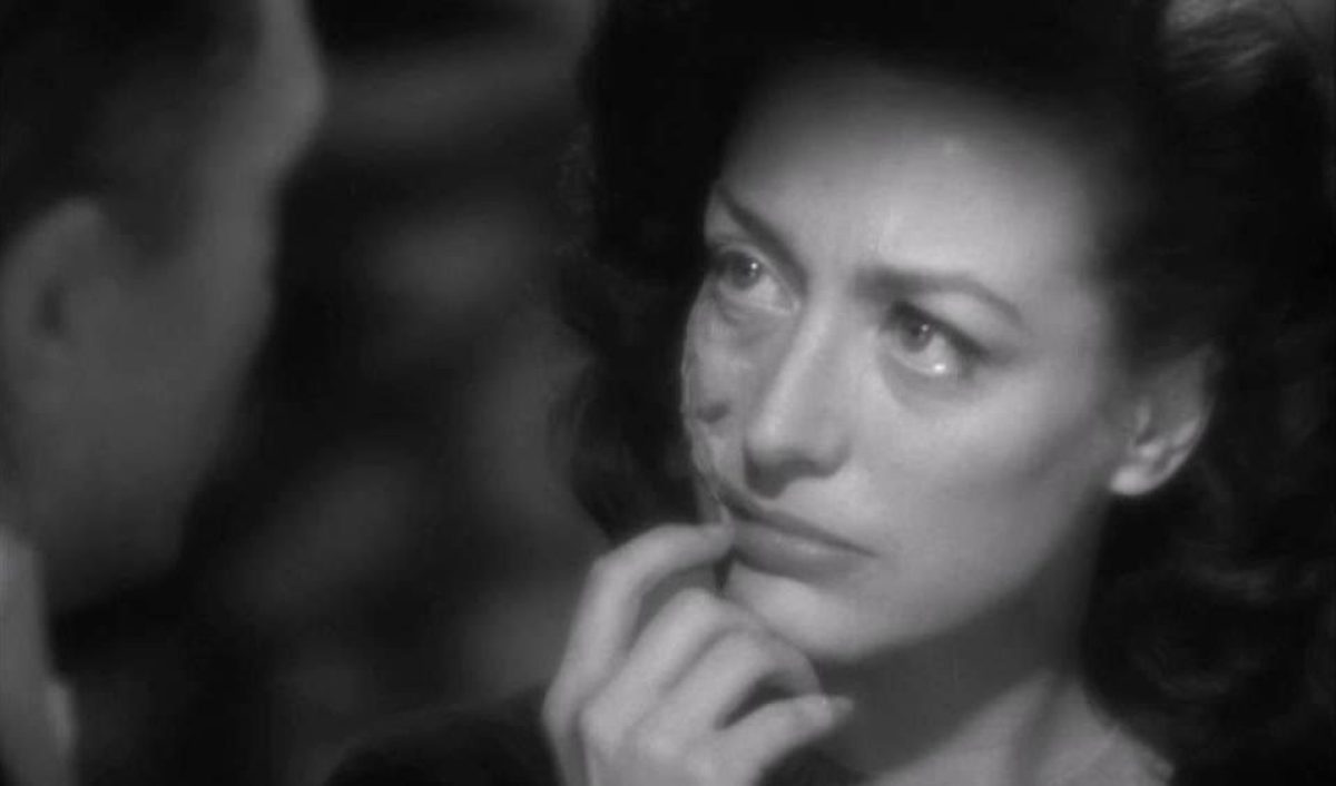 Joan Crawford holds one hand to her disfigured face while cloaked in shadow.