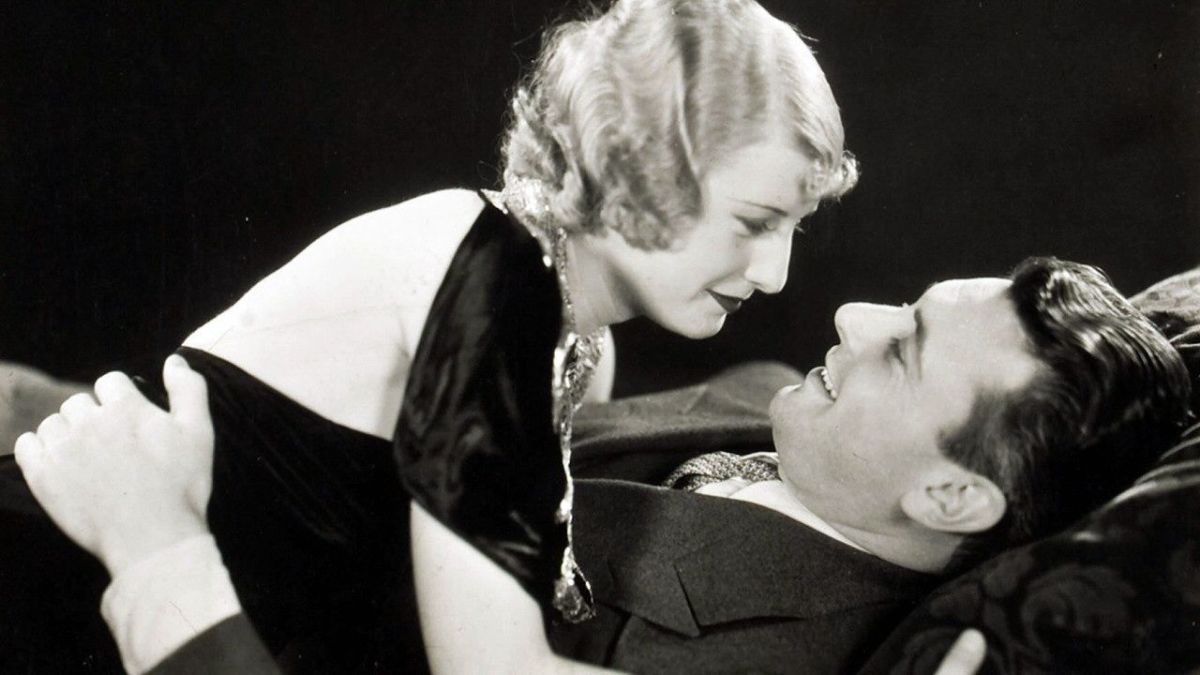 Barbara Stanwyck gazes into the eyes of a man as she lies on top of him.