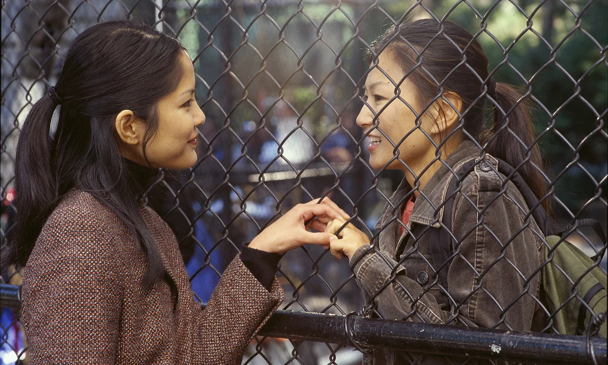 Lynn Chen and Michelle Krusiec hold hands through a fence.