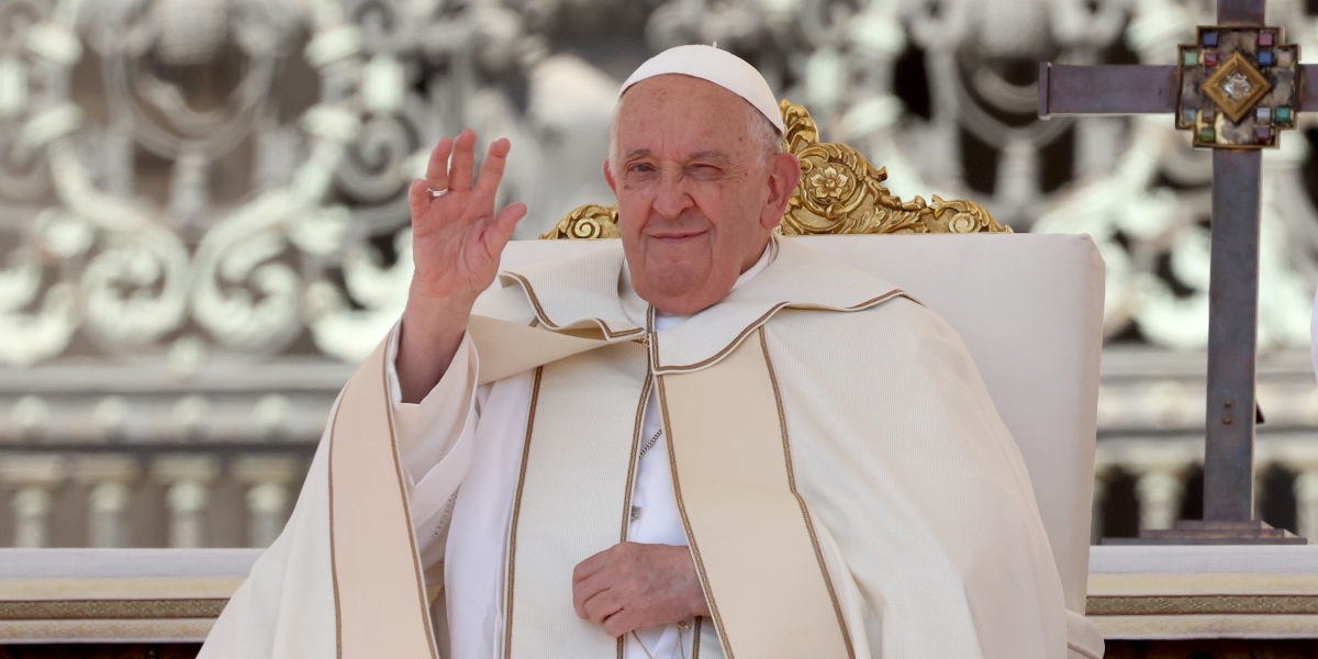 Pope Francis waves toward the camera with one eye squinted