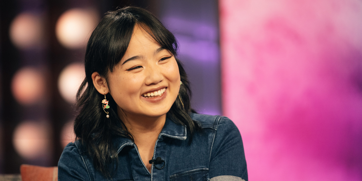 Helen J. Shen smiling in a denim jumpsuit during an interview promoting Maybe Happy Ending