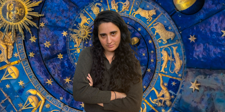 Kayla with her arms crossed with an astrological background