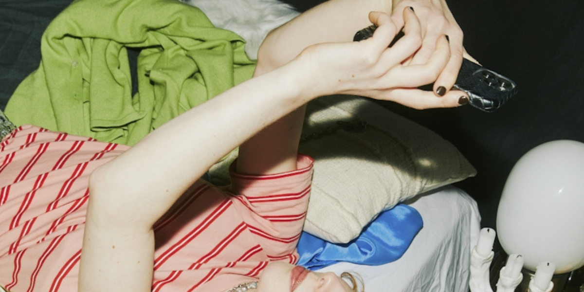 GLAAD 2025 Social Media Safety Index: An abstract photo of a woman lying on her bed looking up at her phone