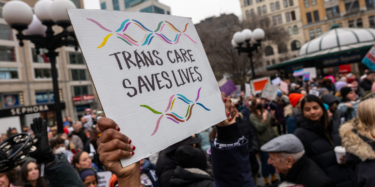 a protest sign that says TRANS CARE SAVES LIVES