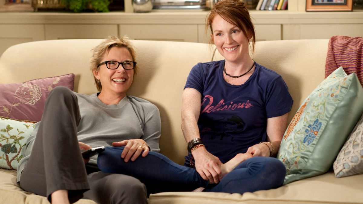 Annette Bening and Julianne Moore laugh next to each other on a couch in The Kids Are All Right