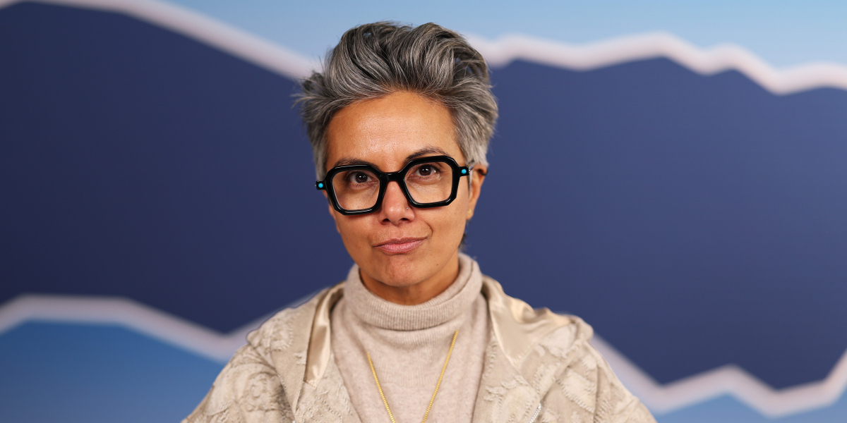 Fawzia Mirza interview: a close up of Fawzia in a tan sweater with a gold chain and thick black glasses