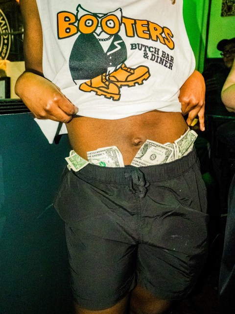 a person's torso and upper legs, with dollar bills stuffed in the waistband of black shorts.