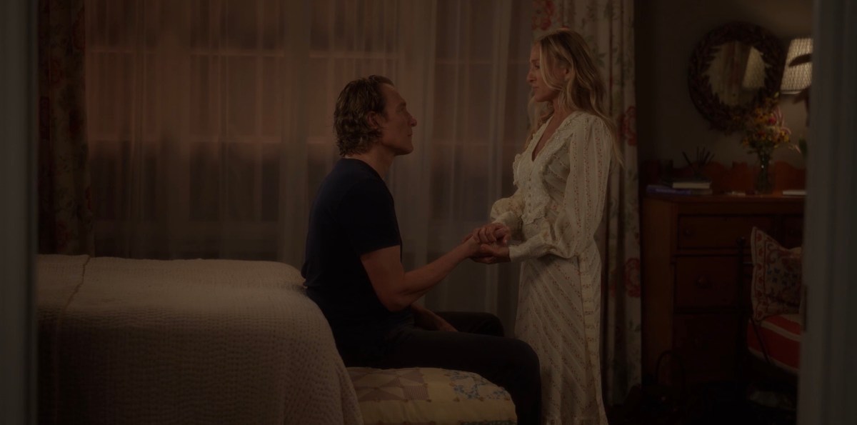 aidan holding carrie's hands while he sits on the bed