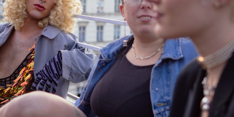 Trans in Dallas: A group of visibly queer people lean against a railing while talking to each other.