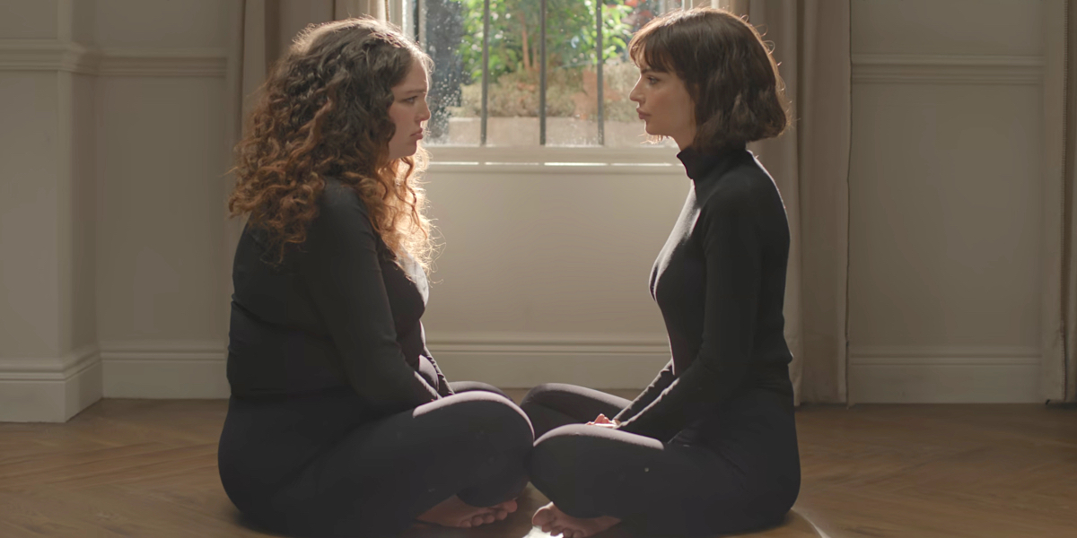 Queer actors Megan Stalter and Emily Ratajkowski look at each other dressed in black in Lena Dunham's Too Much on Netflix
