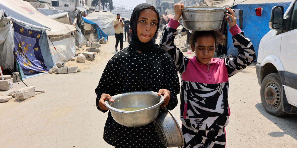 two girls carry pots with soup in Gaza
